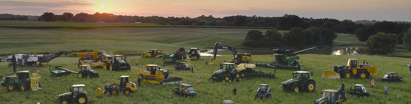 Personnes se déplaçant parmi plusieurs types d’équipements John Deere dans un grand champ.