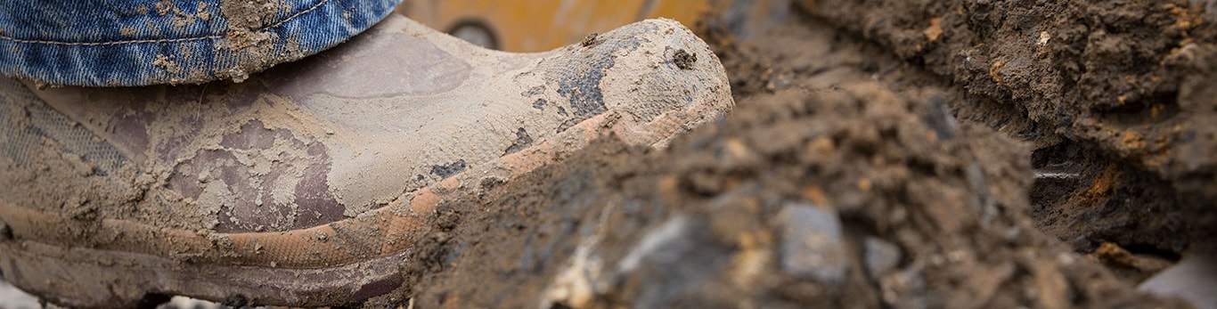 Gros plan d'une botte boueuse sur les traces de passage d'une machine dans la terre