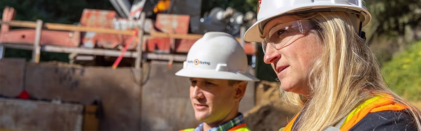 Travailleur et travailleuse portant des casques de sécurité qui regardent de l'équipement de construction