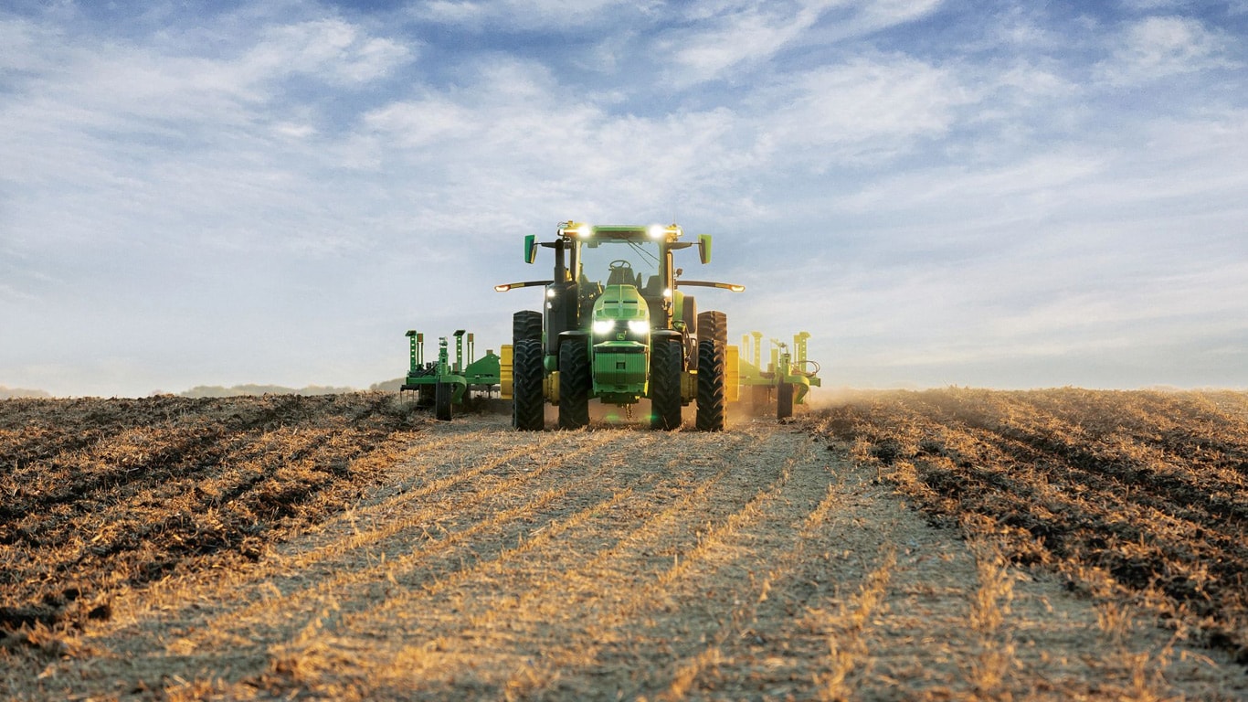 Tracteur John Deere en conduite autonome tractant un équipement de travail du sol dans un champ ouvert.