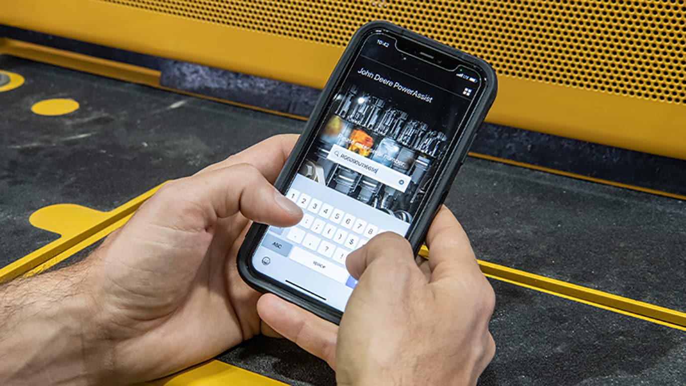Homme tenant un smartphone en main tandis qu’il cherche un numéro de série de moteur dans l’application PowerAssist John Deere