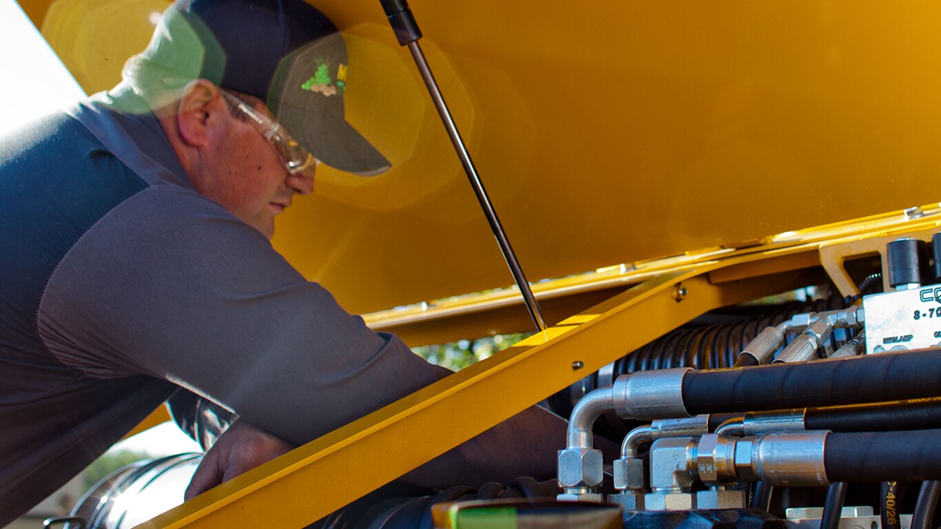 homme travaillant sur un moteur sous un capot jaune