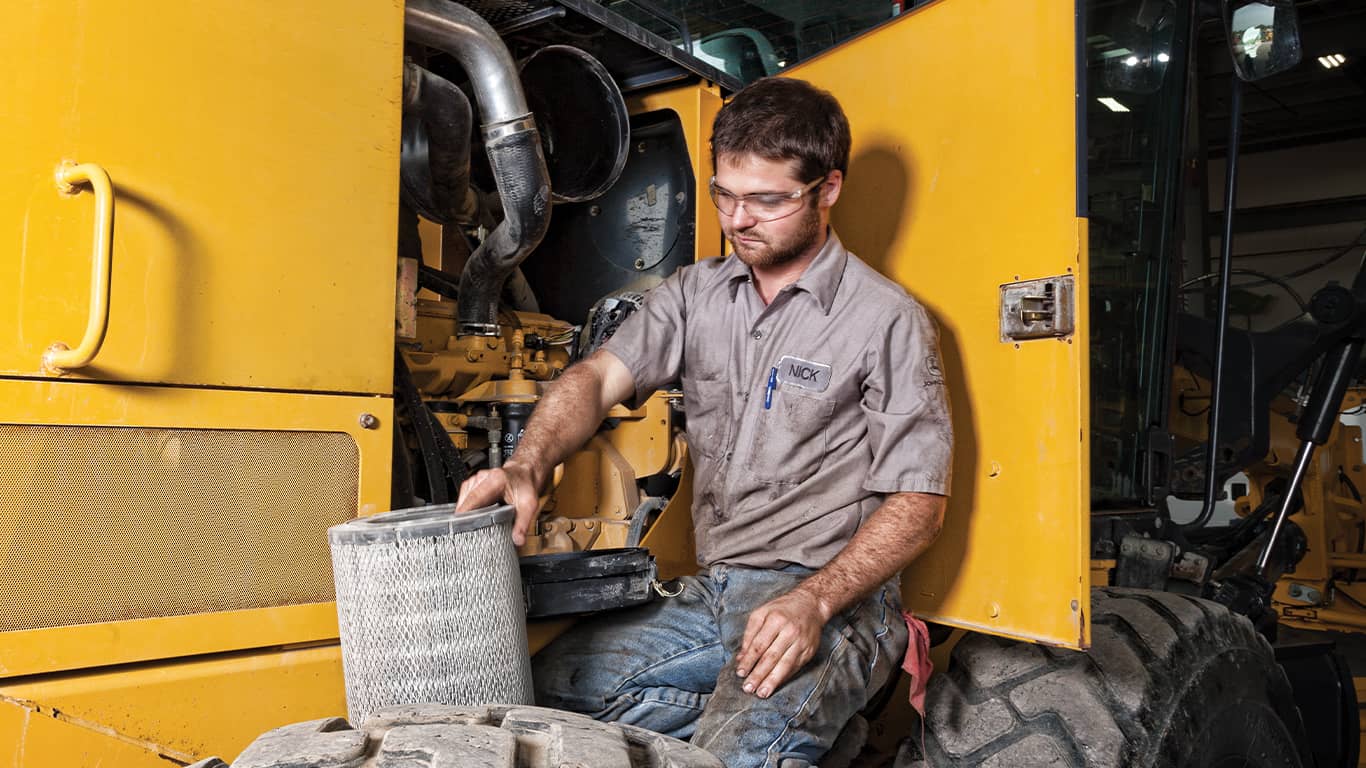 Homme portant des lunettes de sécurité et travaillant sur un moteur John Deere à l’intérieur d’une machine d’équipement lourd