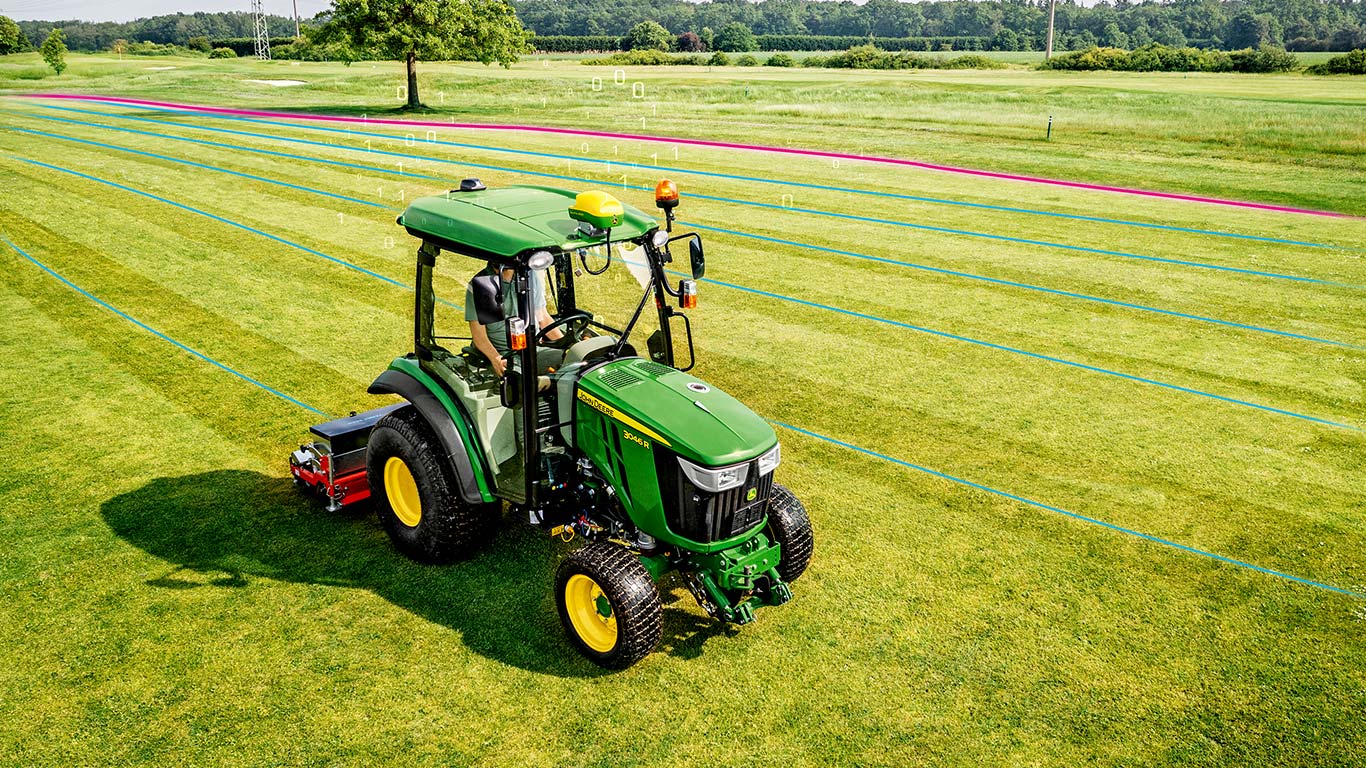 Greenkeeper passant un tracteur compact John Deere sur le gazon.