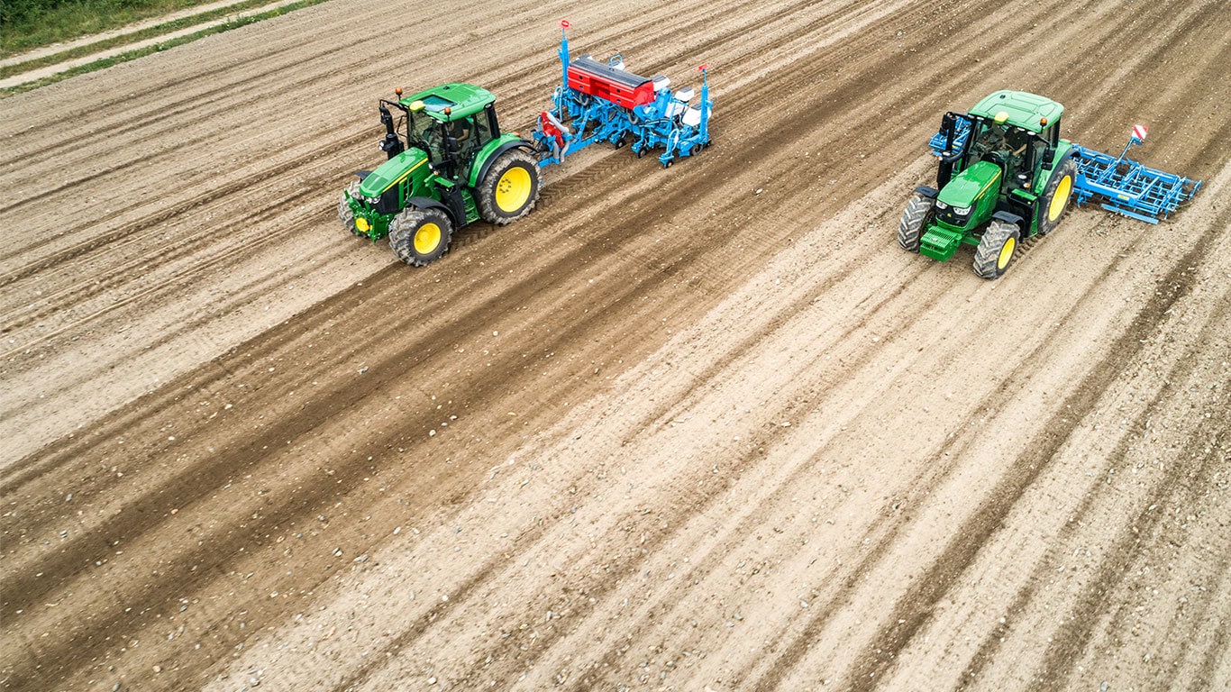 Deux tracteurs John Deere 6M sur un champ de terre battue. L’un tire un semoir de précision Monsomen. L’autre tire un combiné de lit de semences Lemken