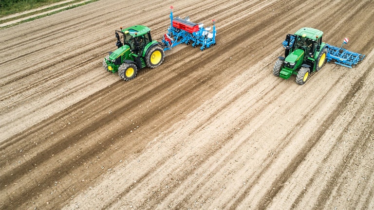 Deux tracteurs John Deere 6M sur un champ de terre battue. L&rsquo;un tire un semoir de pr&eacute;cision Monsomen. L&rsquo;autre tire un combin&eacute; de lit de semences Lemken