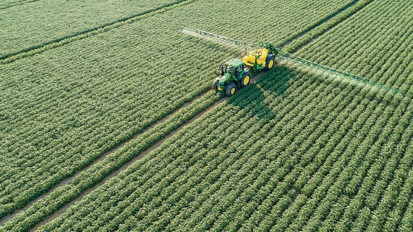 Tracteur John Deere de la s&eacute;rie 6M tirant un pulv&eacute;risateur remorqu&eacute; M700 dans un champ de pommes de terre