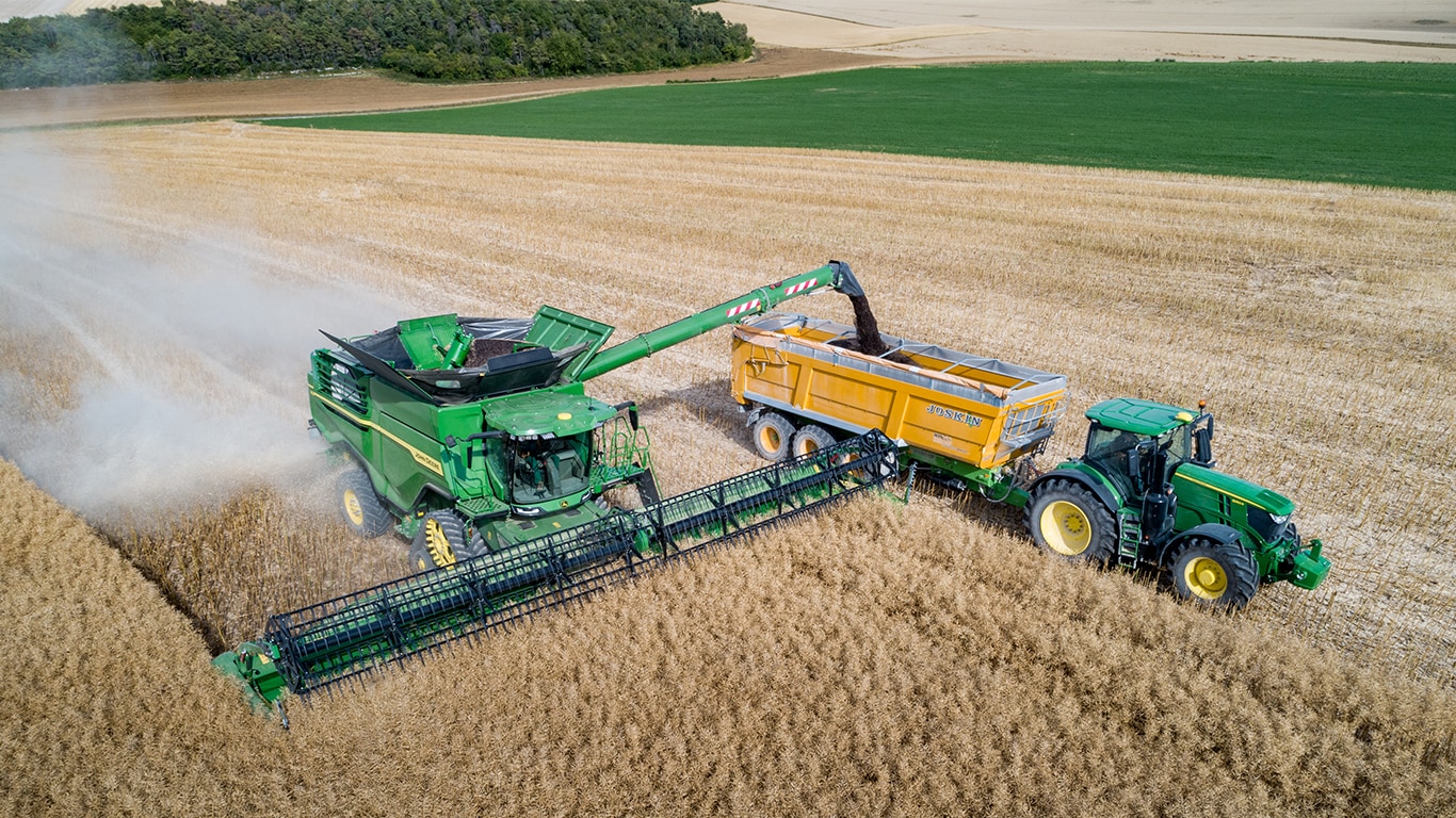 Moissonneuse-batteuse John Deere série X déchargeant du colza dans un chariot à grain tiré par un tracteur John Deere